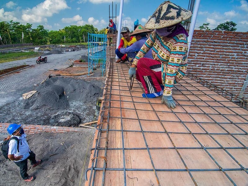 Pekerja merangkai besi tulangan pelat lantai di atas dinding bata sebuah rumah yang sedang dibangun