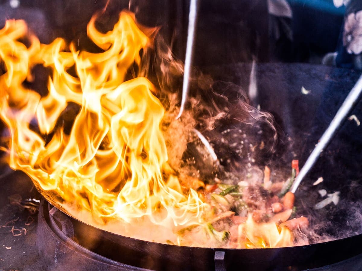 Kobaran api dari wajan besar saat juru masak menumis sayuran dan daging