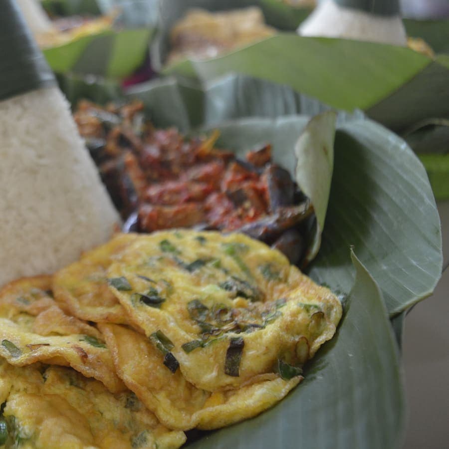 Nasi tumpeng dengan telur dadar iris dan sambal goreng beralas daun pisang