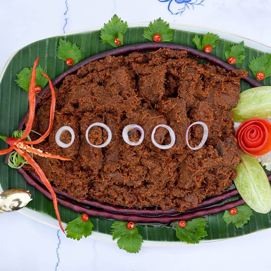 Rendang daging sapi di atas piring beralas daun pisang dengan pelengkap sayuran