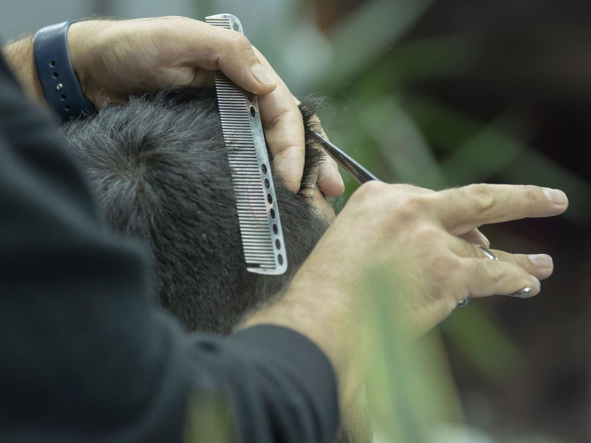 Tangan penata rambut memotong rambut pelanggan dengan sisir dan gunting